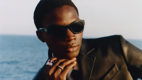 Mannequin portant une veste foncée et des lunettes de soleil, photographié près de l’eau.